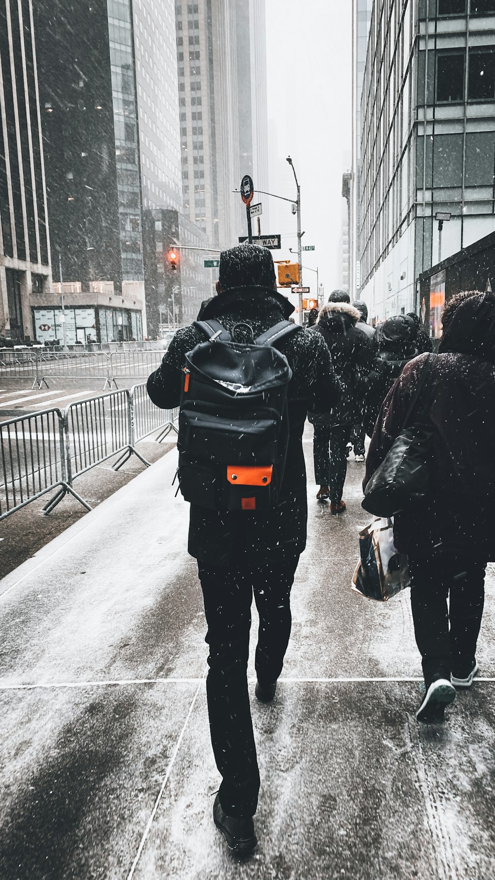 man in black jacket and black pants carrying black backpack walking on snow covered road during