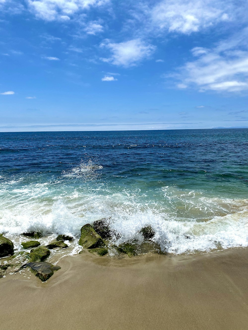 sea waves crashing on rocks under blue sky during daytime