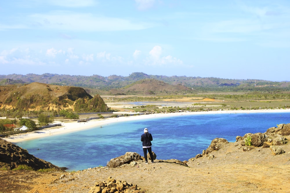 man in black jacket standing on brown rock near body of water during daytime