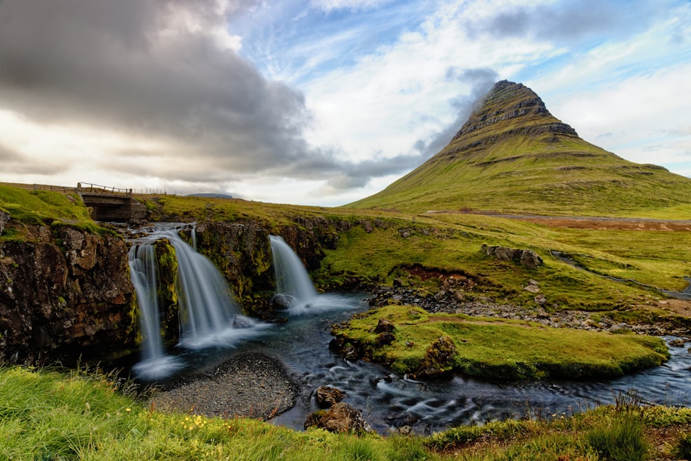 green grass field near waterfalls under cloudy sky during daytime