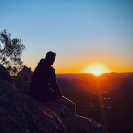 silhouette of man sitting on rock during sunset