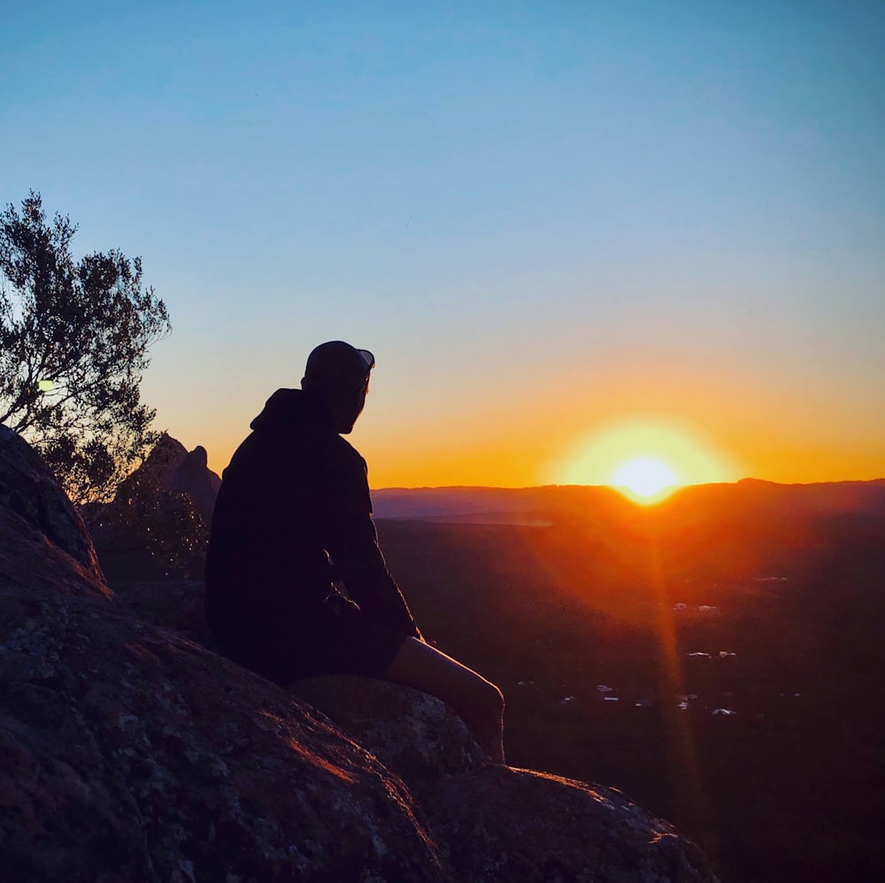 silhouette of man sitting on rock during sunset