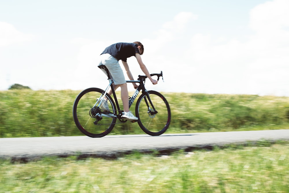 낮 동안 회색 아스팔트 도로에서 검은 산악 자전거를 타고 검은 셔츠를 입은 남자
