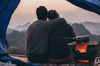 man and woman sitting on sand near bonfire during daytime