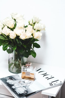 A fresh bouquet of white roses next to a bottle of light floral perfume.