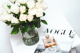 An elegant glass vanity featuring m.y makeup perfumes surrounded by fresh white roses.