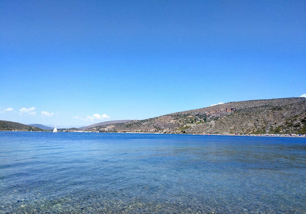 mare blu vicino alla montagna verde sotto il cielo blu durante il giorno