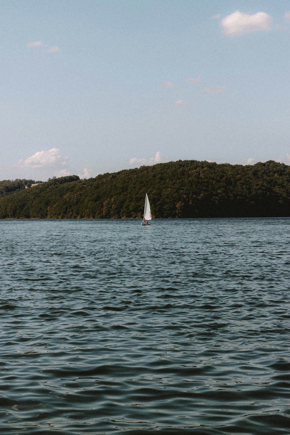 white sailboat on sea near green mountain during daytime