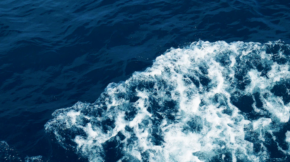 Large wave crashes onto the shore in a close-up ocean view from above