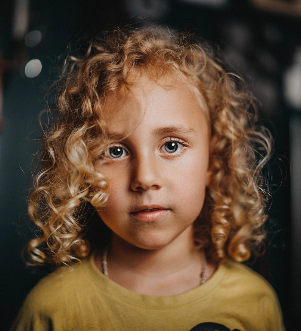 A girl in a yellow shirt with long hair, looking away from the camera.