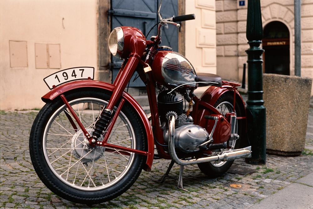 red and black standard motorcycle parked beside brown concrete building