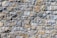 A close-up view of a textured stone wall, with irregularly shaped stones in varying shades of gray and brown, meticulously fitted together to form a solid structure.