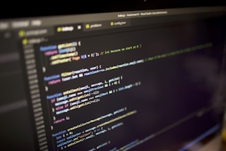 Close-up view of a computer screen displaying a code editor with JavaScript code. The code is color-coded, showing various functions, variables, and comments. The editor interface includes tabs and a menu bar, indicating an active coding session.