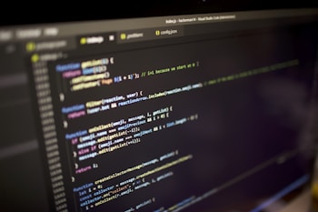 Close-up view of a computer screen displaying a code editor with JavaScript code. The code is color-coded, showing various functions, variables, and comments. The editor interface includes tabs and a menu bar, indicating an active coding session.