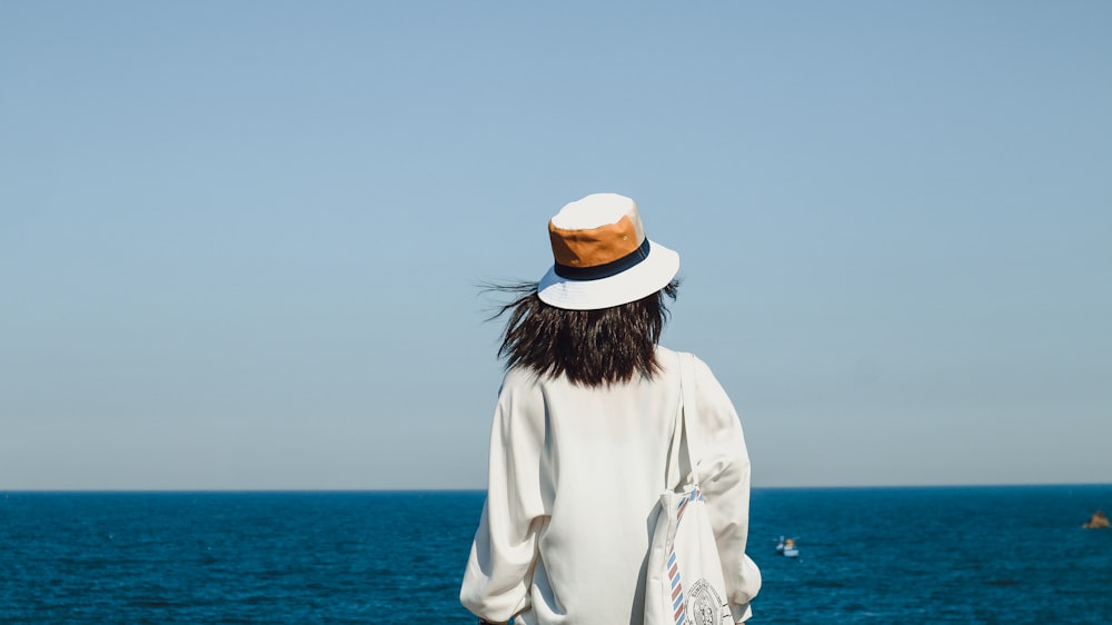 woman in white long sleeve shirt wearing white hat standing on beach during daytime