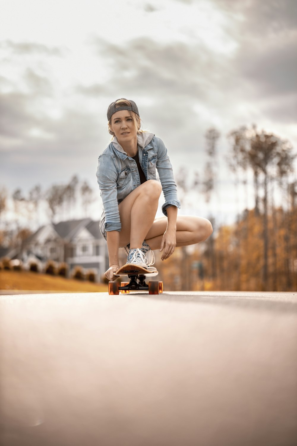 woman in gray denim jacket and black pants sitting on brown skateboard during daytime