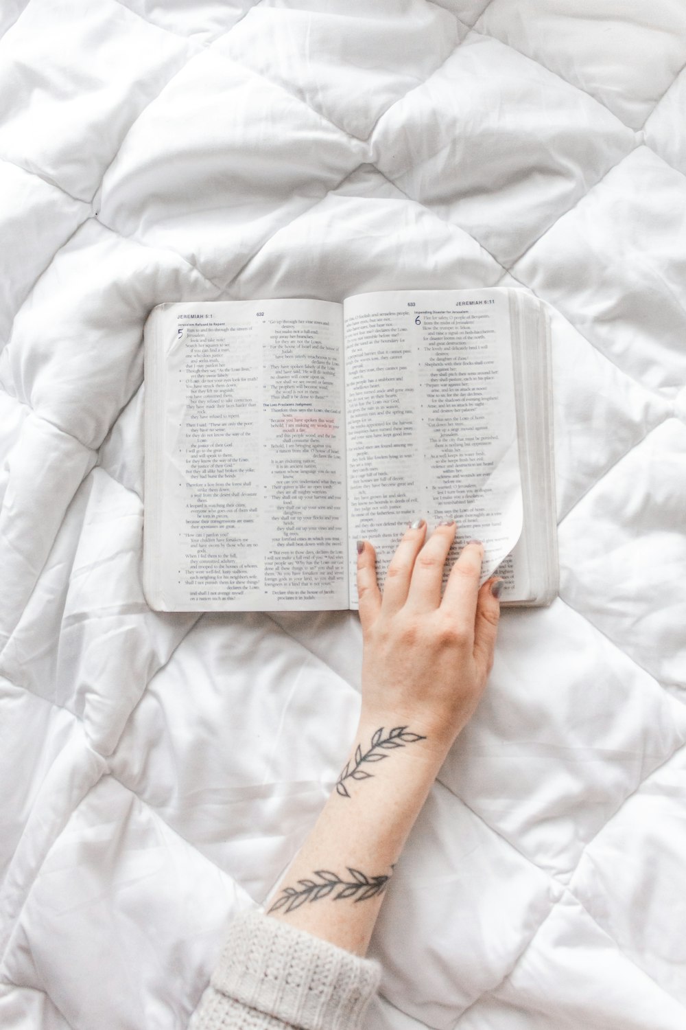 personne lisant un livre sur un lit blanc