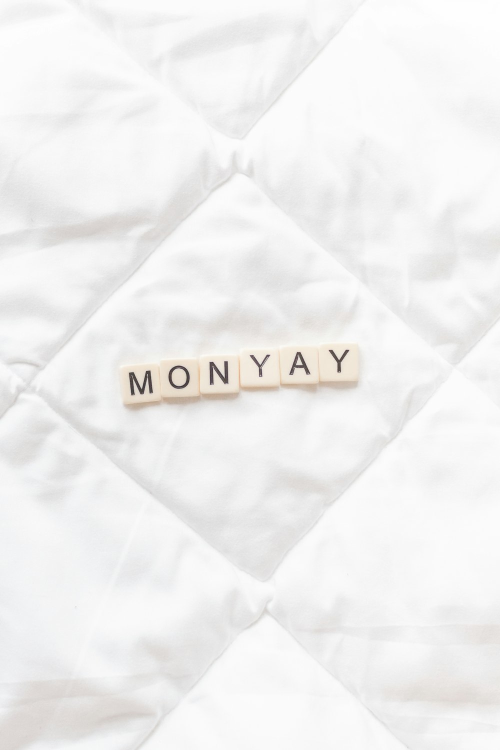 the word monday spelled with scrabbles on a white quilt