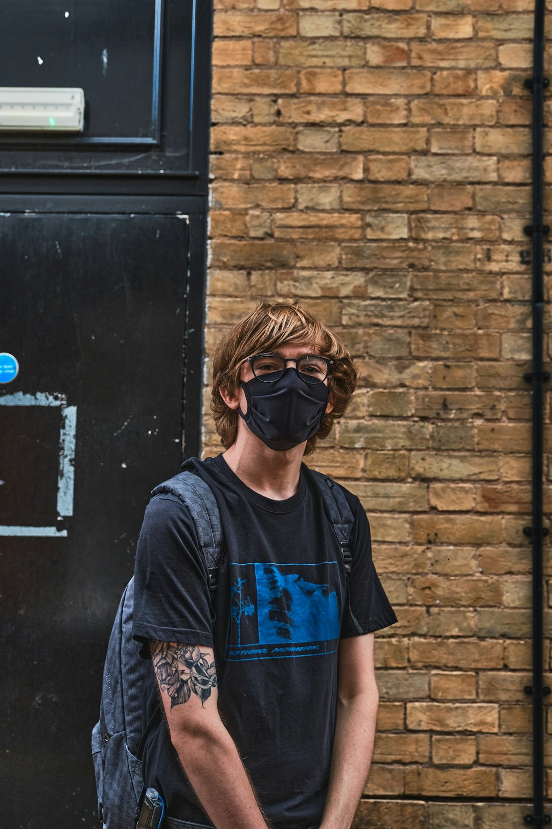 man in blue crew neck t-shirt wearing black sunglasses standing beside black door