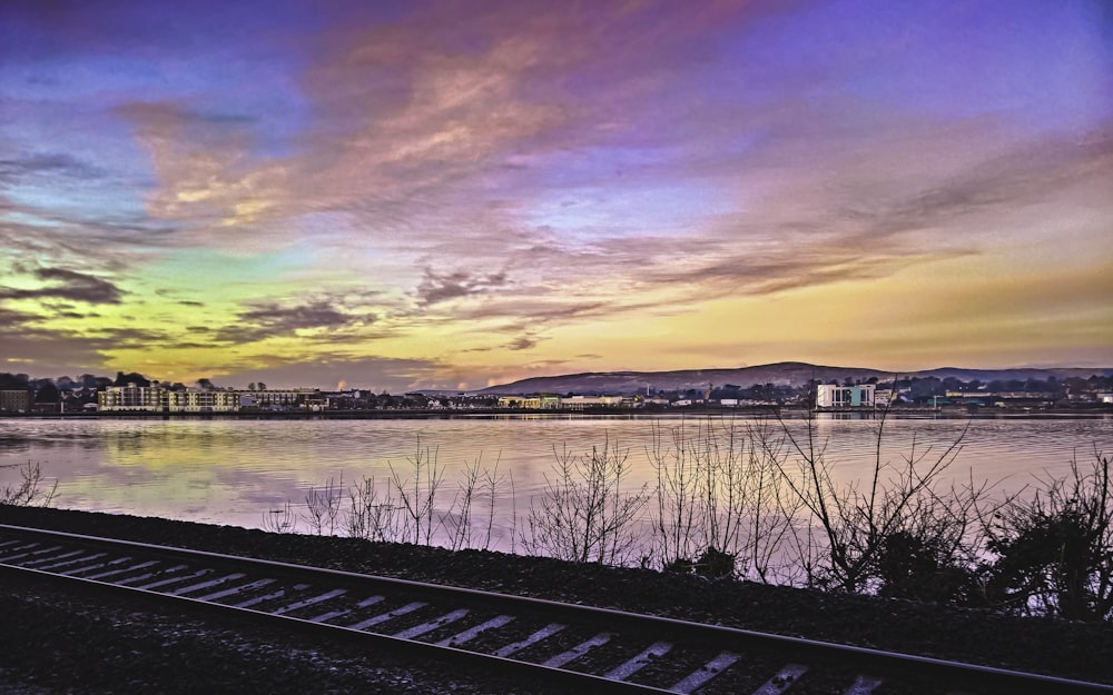 black train rail near body of water during sunset