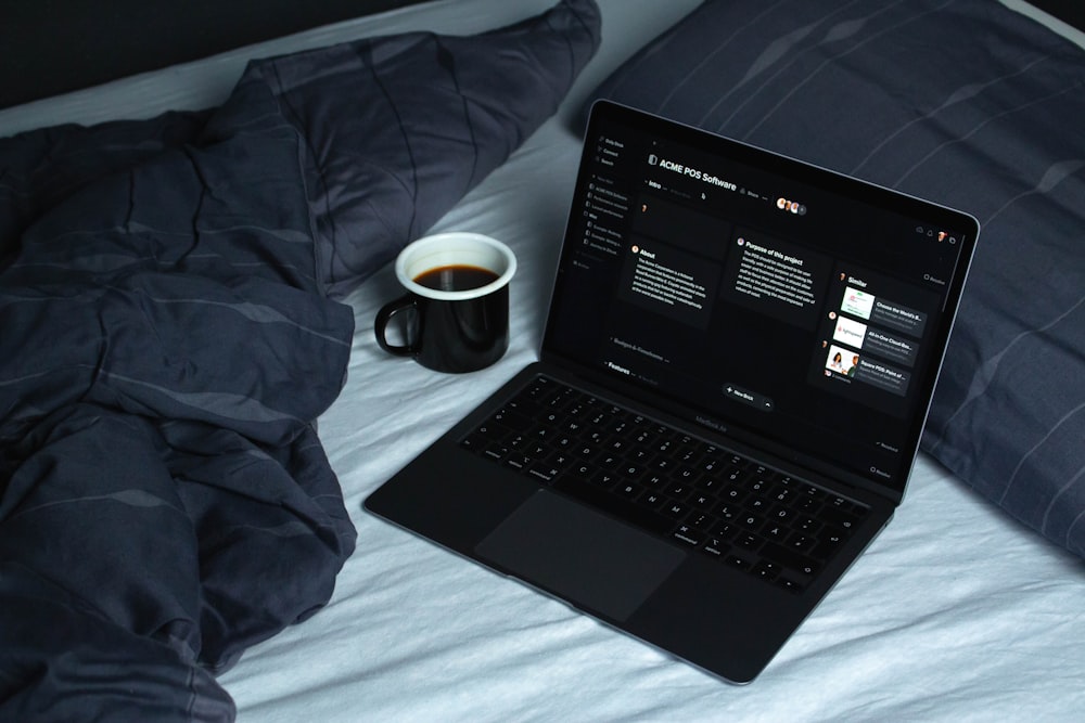 black laptop computer on white bed