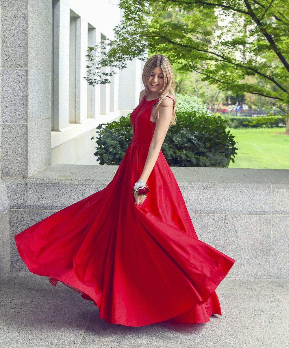 donna in vestito rosso senza maniche in piedi sul pavimento di cemento grigio durante il giorno