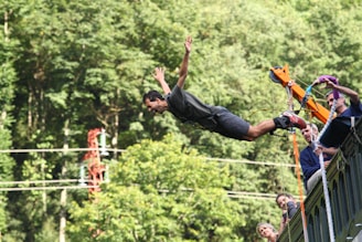 man in black t-shirt and blue denim jeans jumping on mid air during daytime
