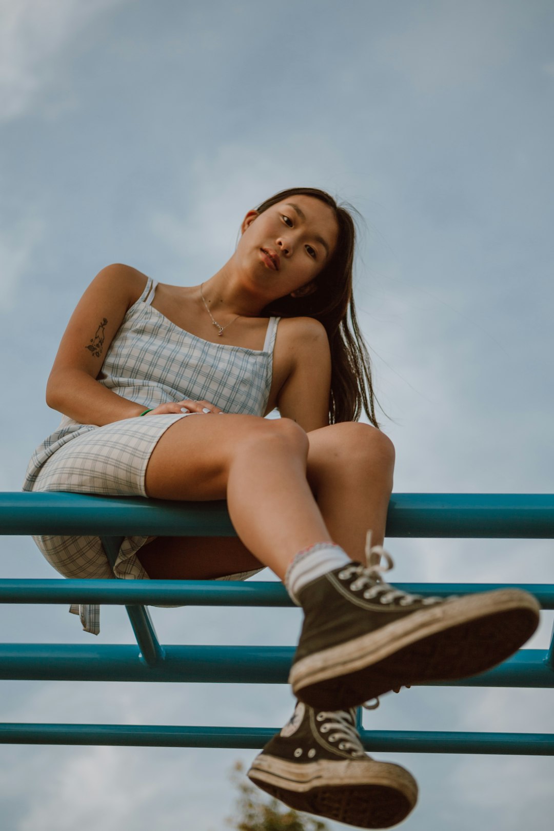 woman in white and black plaid dress shirt and blue denim shorts sitting on blue metal