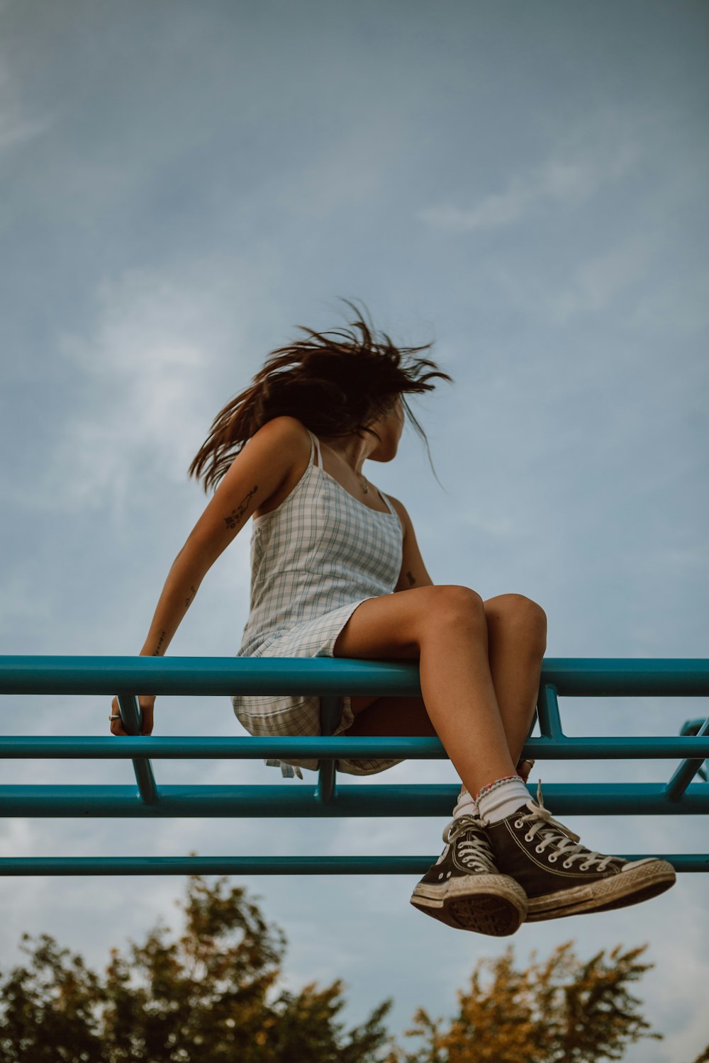 woman in white tank top and blue denim shorts sitting on blue metal railings during daytime