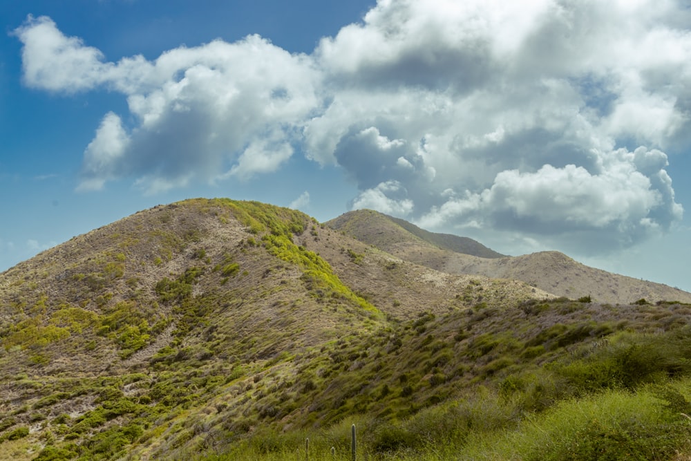 Grünes Grasfeld und Berg unter weißen Wolken und blauem Himmel tagsüber