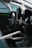 The interior of a car is shown, featuring a black steering wheel with a racing design and paddle shifters. The surrounding area includes a roll cage and carbon fiber elements, indicating it is a racing vehicle. A digital display is partially visible in the driver's dashboard area.