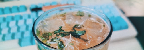 A close-up of hands holding a glass of infused water with fresh herbs.