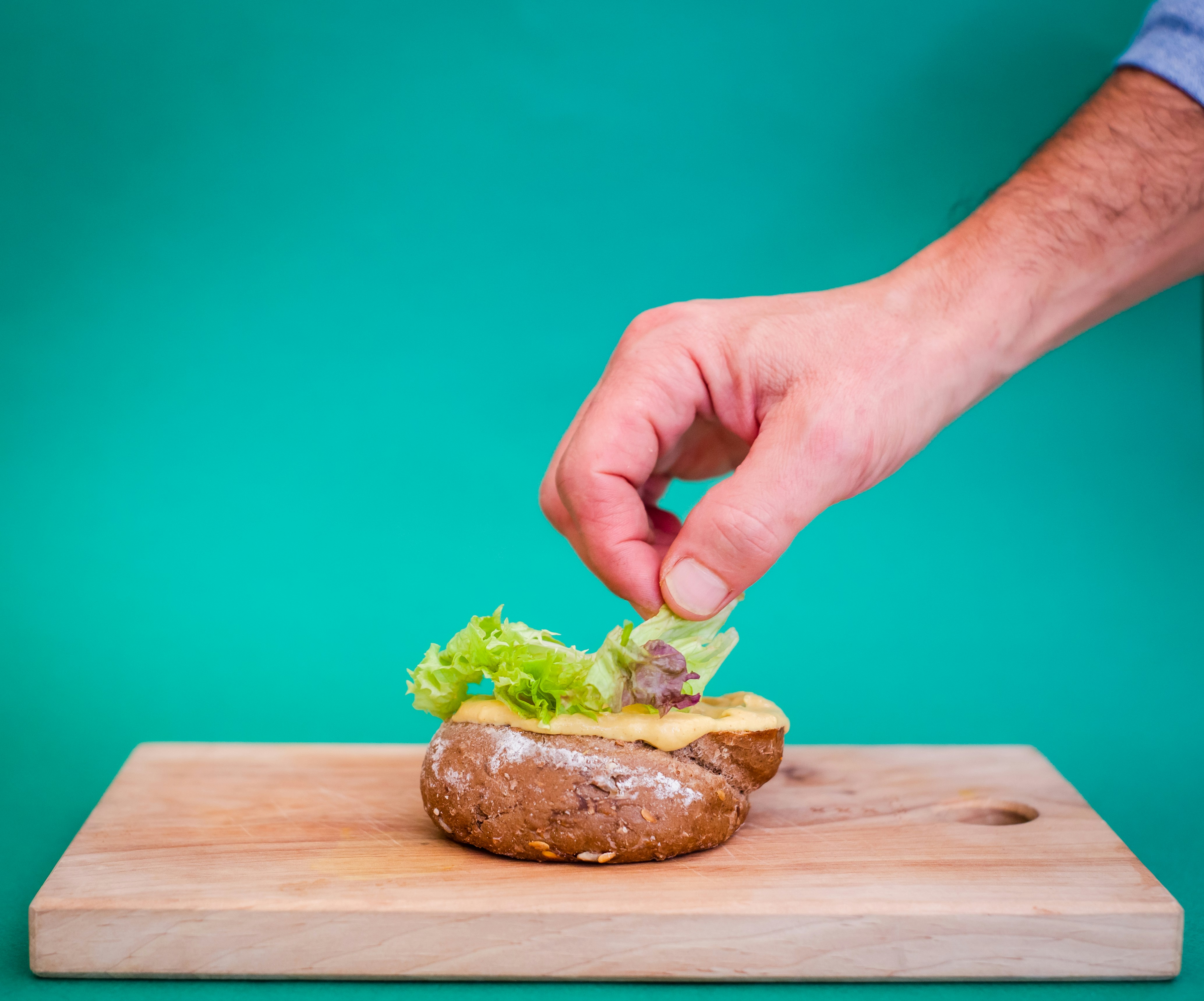 Hand placing lettuce on a burger