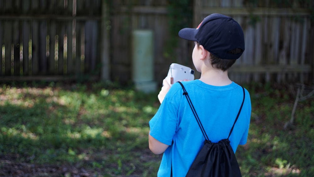 boy in blue crew neck t-shirt and black cap standing on green grass field during