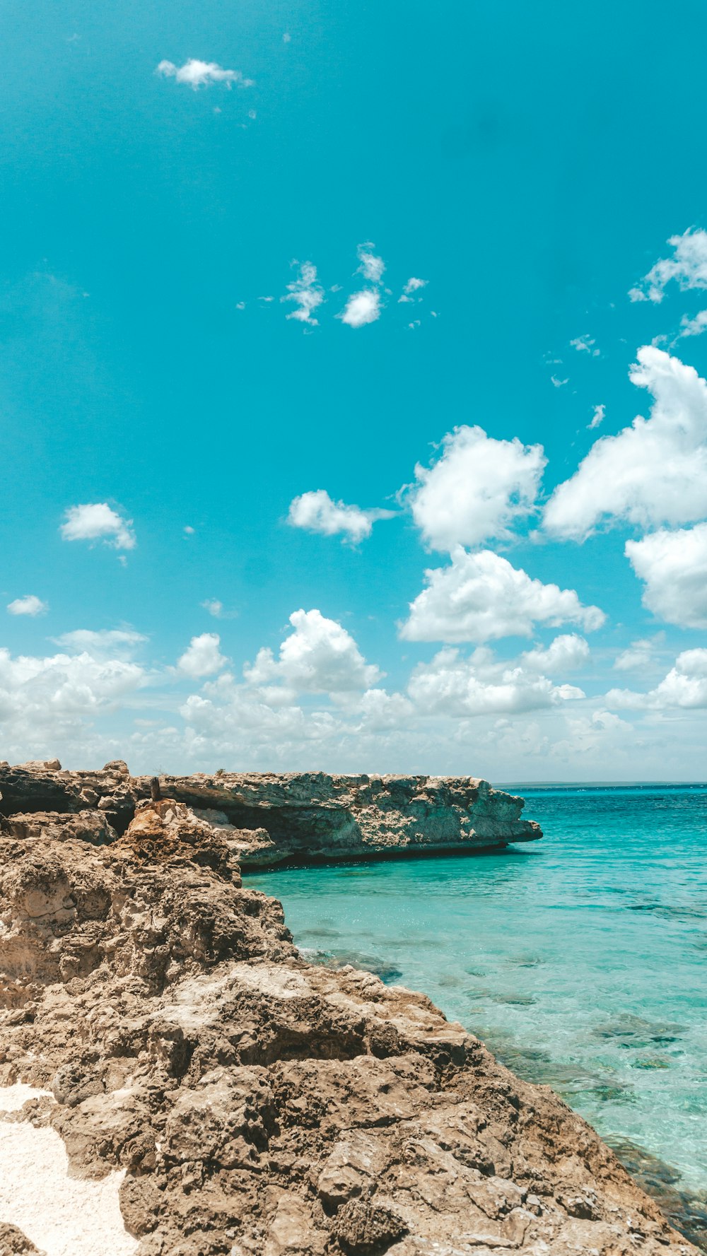 brown rock formation beside blue sea under blue sky and white clouds during daytime