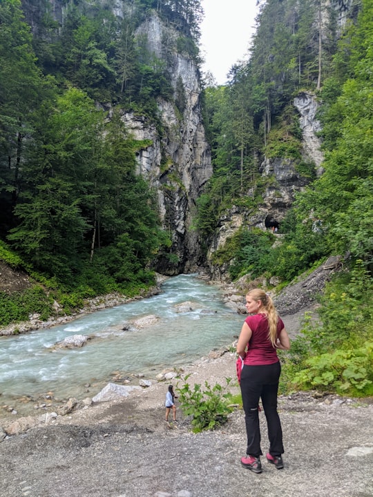 woman in black tank top and black pants standing on rocky road near river during daytime in Partnachklamm Germany