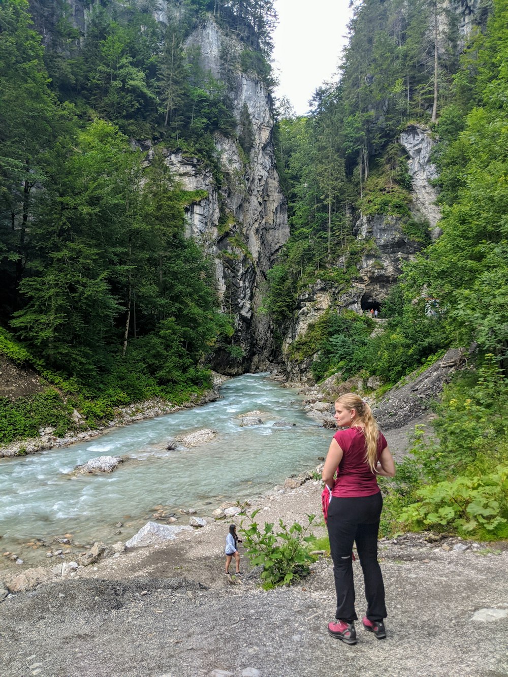 woman in black tank top and black pants standing on rocky road near river during daytime