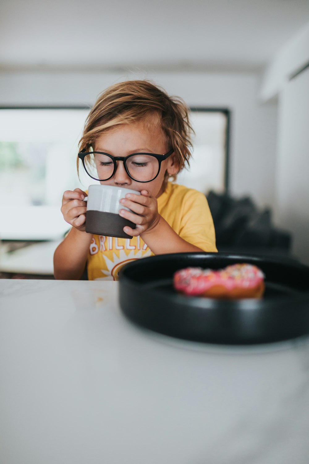 boy in yellow shirt drinking from black ceramic mug