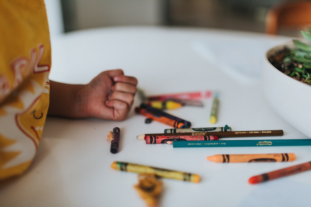 person holding coloring pencils on white table