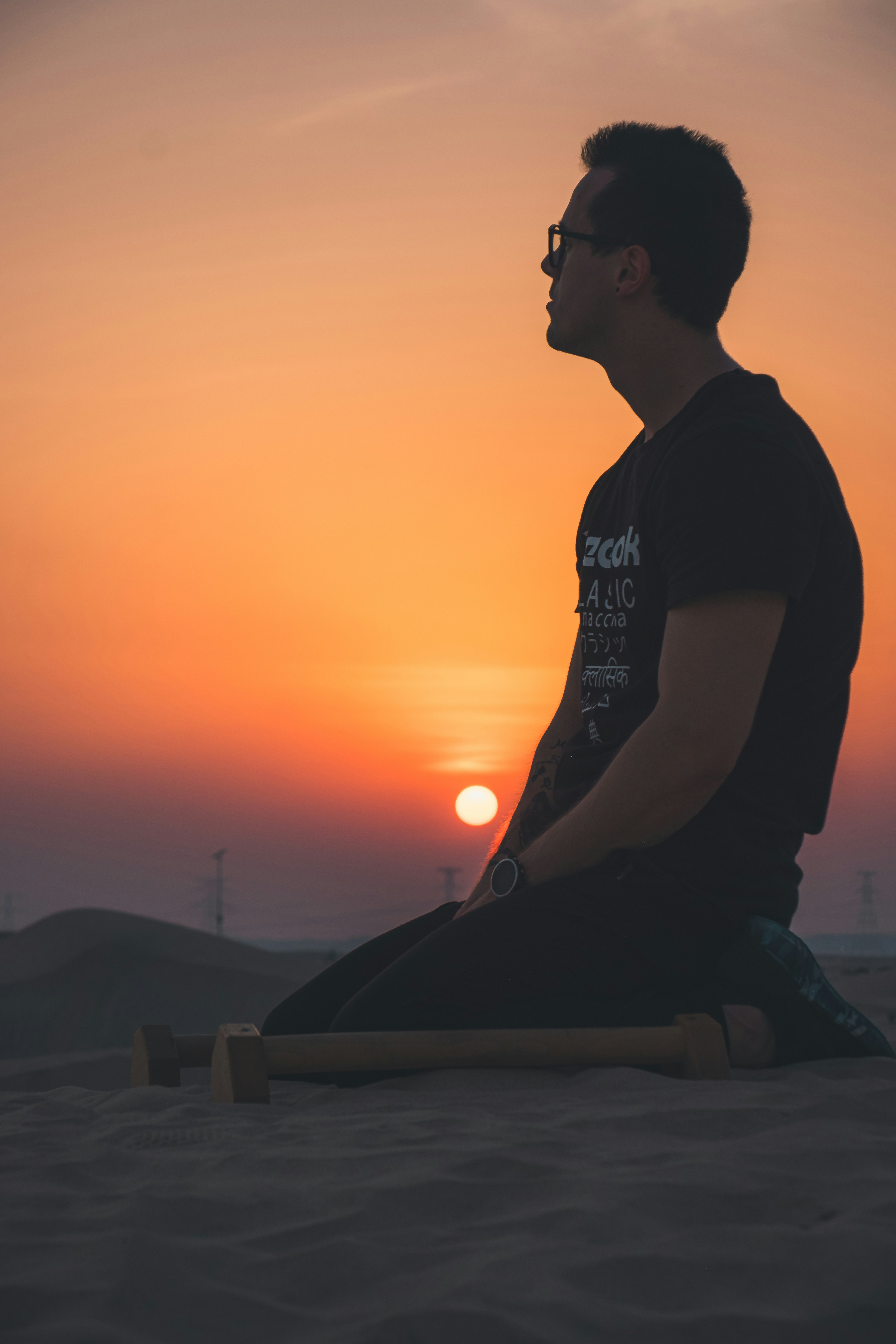 man in black crew neck t-shirt sitting on gray concrete bench during sunset