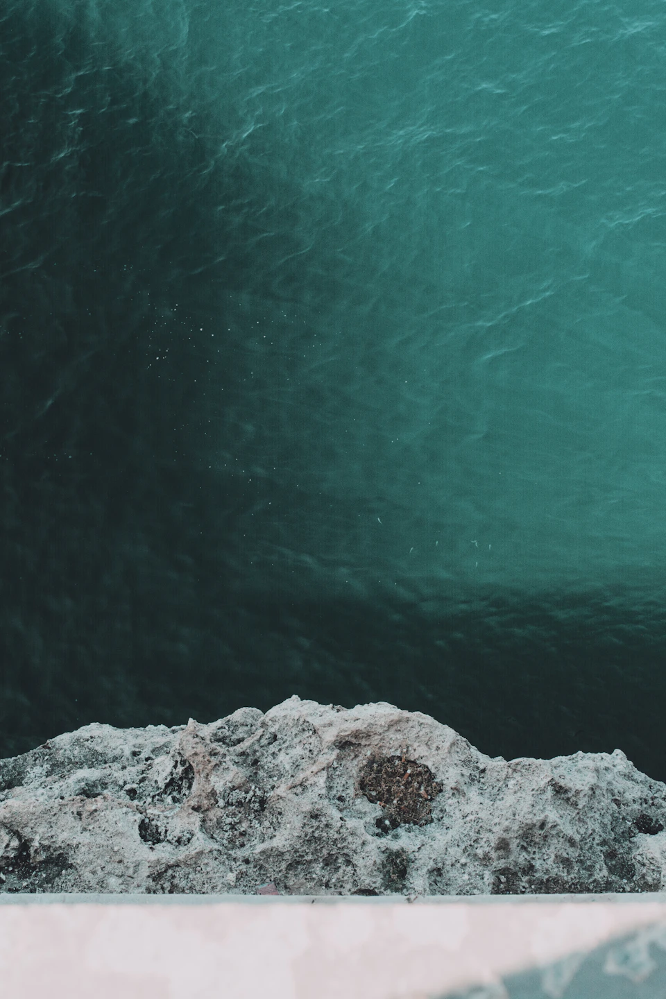Serene cliff overlooking a body of water with moss-covered surface and mirrored blue-green hues
