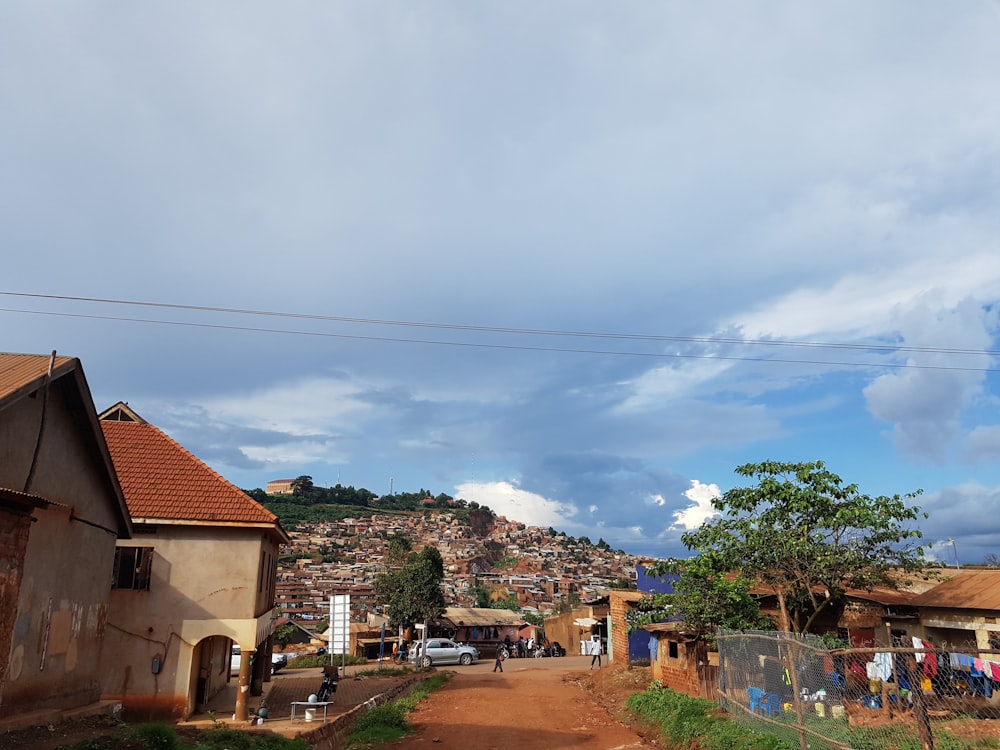 green trees near houses under white clouds and blue sky during daytime