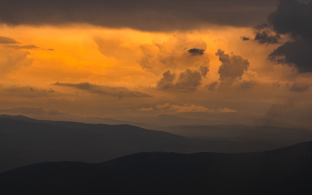 silhouette of mountains under cloudy sky during sunset