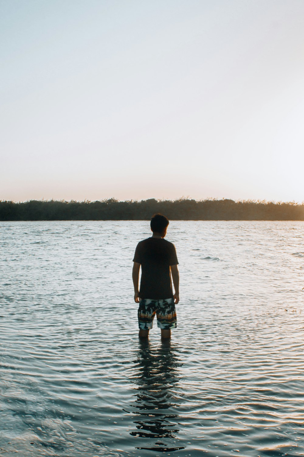 uomo in canotta nera e pantaloncini di jeans blu in piedi sull'acqua durante il giorno