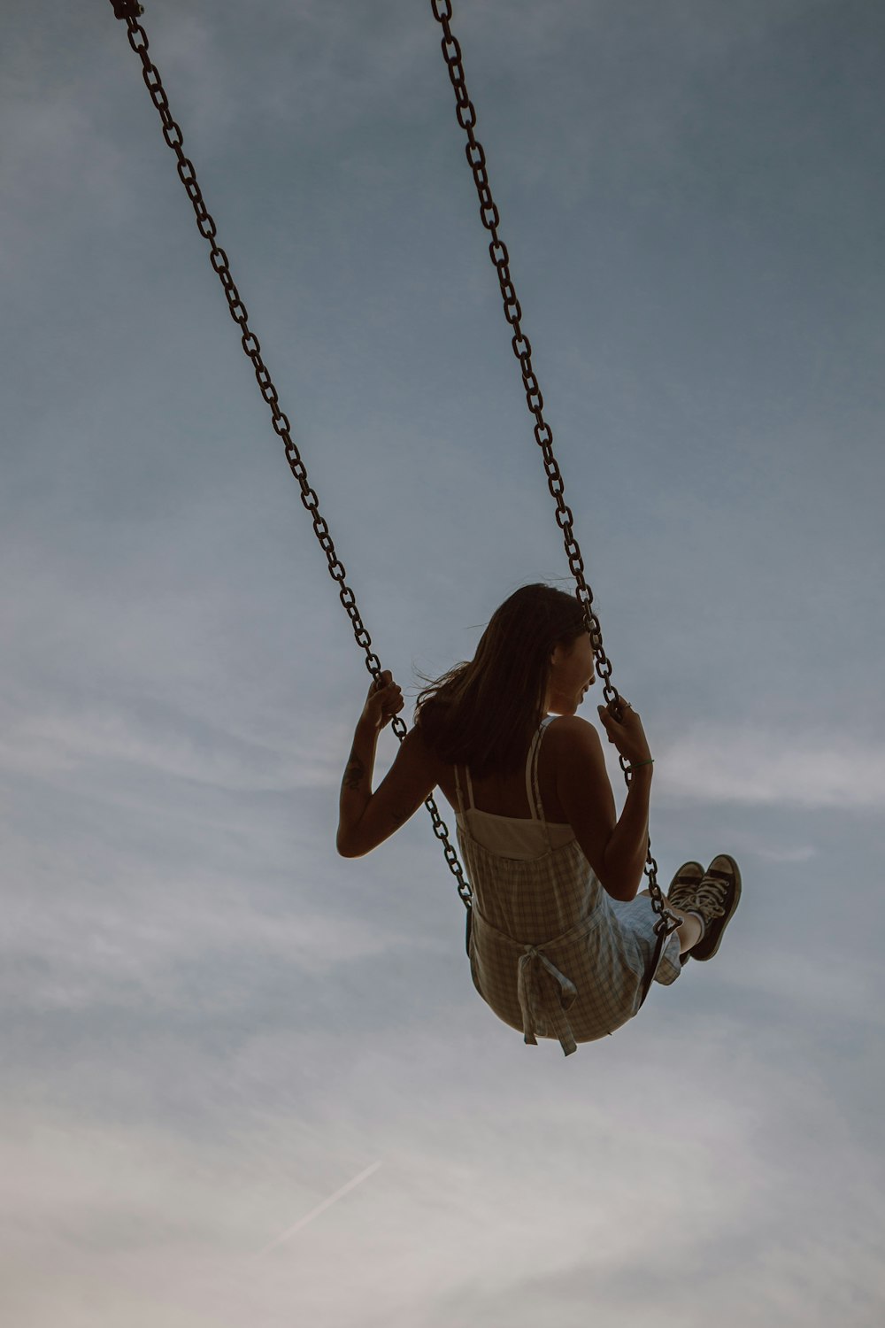 woman in white dress sitting on swing under cloudy sky during daytime