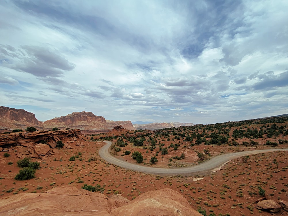 brown dirt road between brown field under white clouds and blue sky during daytime