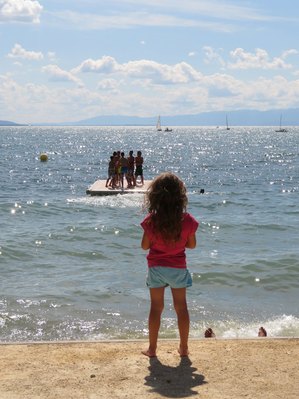 girl in pink shirt and green shorts standing on beach shore during daytime