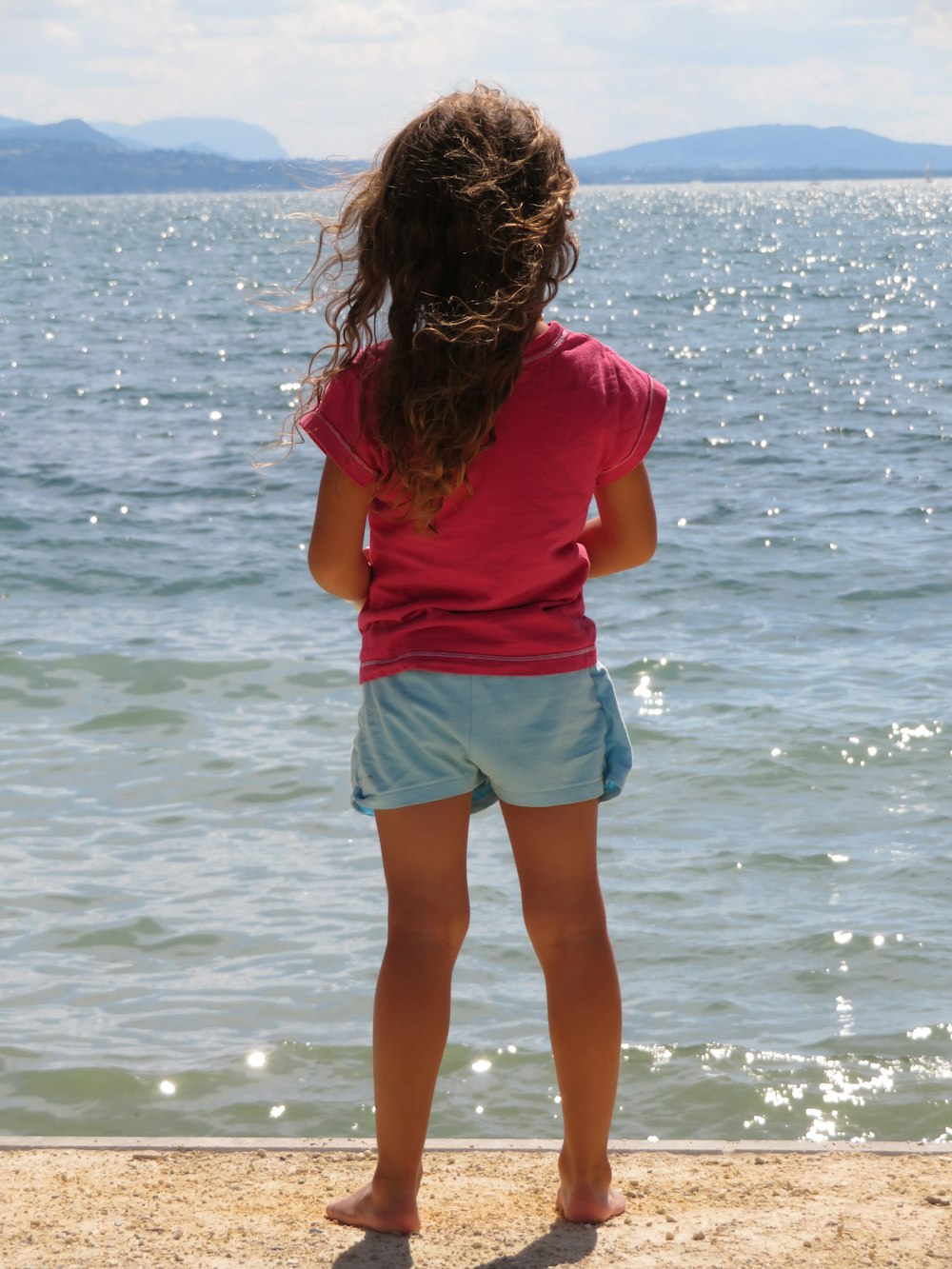 woman in pink shirt and blue denim shorts standing on seashore during daytime
