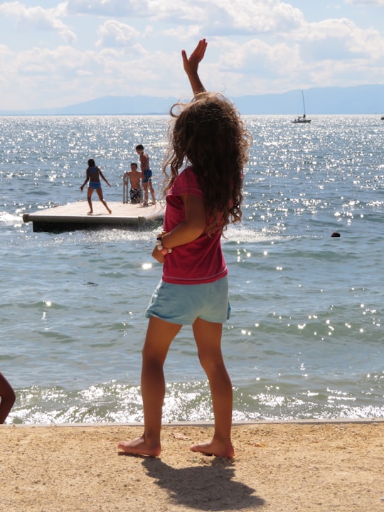 woman in pink tank top and blue denim shorts standing on beach shore during daytime in Lutry Switzerland