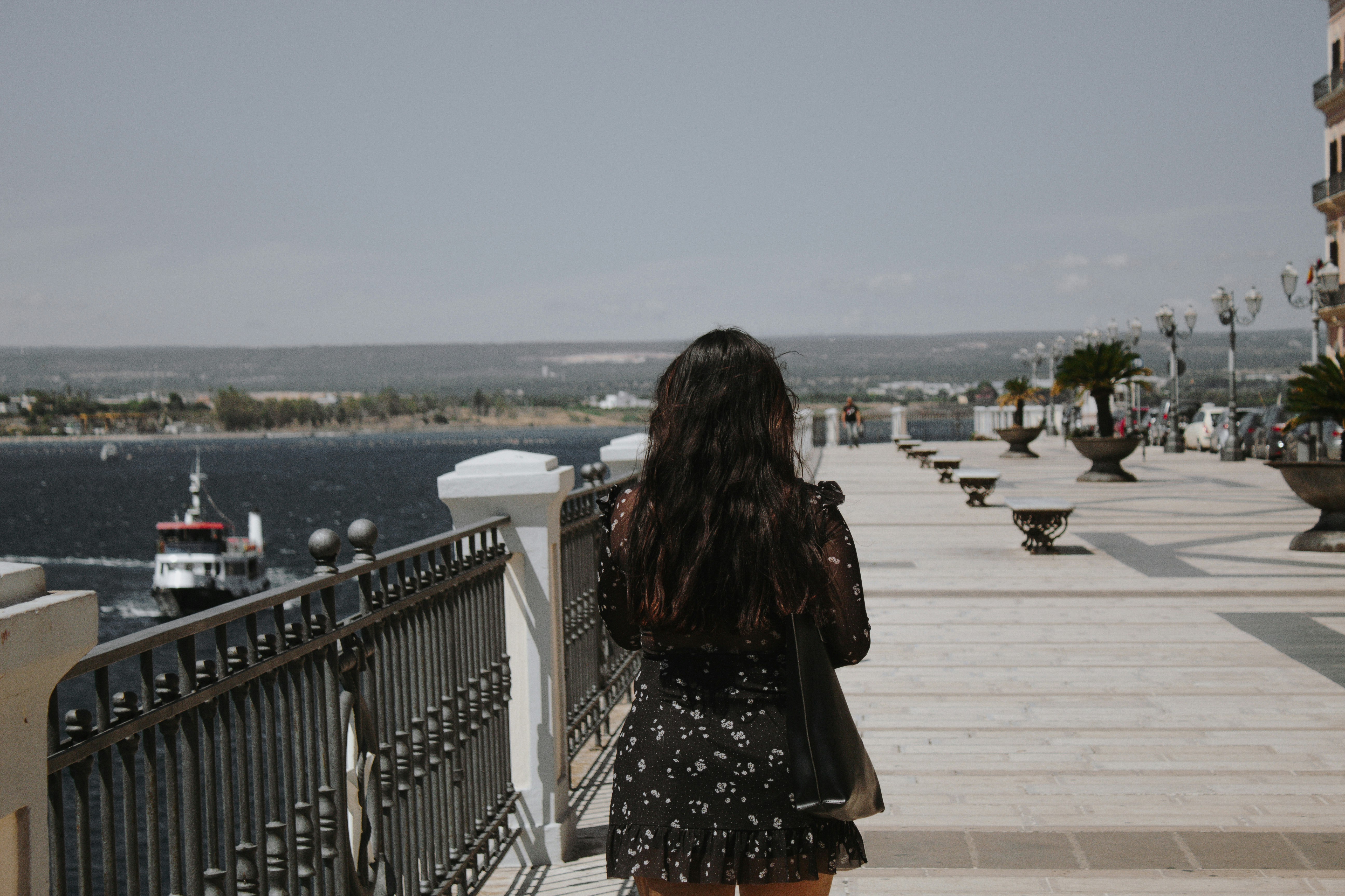 woman in black and white floral dress standing on white concrete bridge during daytime